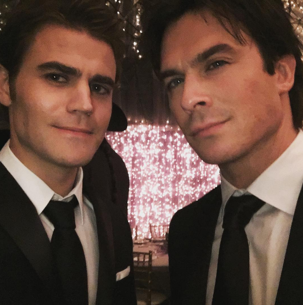 Selfie de Paul Wesley e Ian Somerhalder; os atores usam ternos pretos com camisa social branca e gravata preta, eles sorriem levemente para câmera