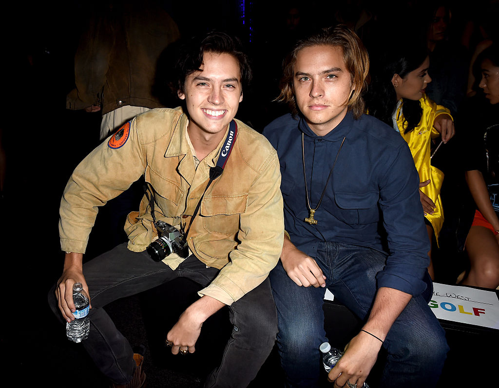 Cole e Dylan Sprouse em desfile do Made LA, em Los Angeles, em 2016; Cole sorri abertamente enquanto Dylan sorri levemente; os dois estão sentados e Cole está com o cabelo preto e Dylan loiro