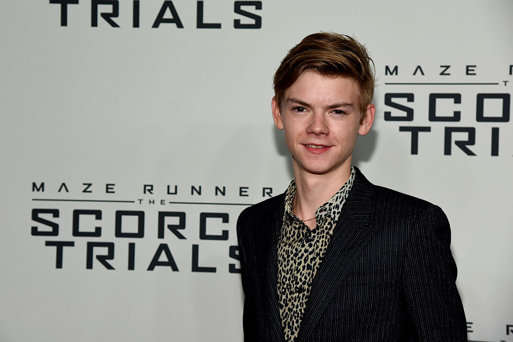 Thomas Brodie-Sangster posando em premiere de The Maze Runner; o ator usa um blazer preto e camisa com estampa de onça enquanto sorri