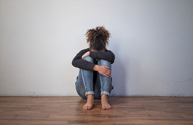 A solidão da garota negra machuca Foto de uma menina negra chorando e escondendo o rosto, sentada no chão
