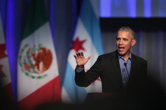 Barack Obama com a mão levantada enquanto fala em discurso; ele usa terno preto com uma camisa azul