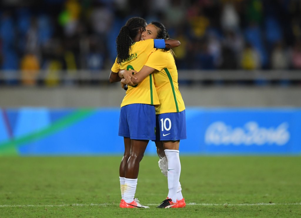 Mulheres se abraçam em campo de futebol