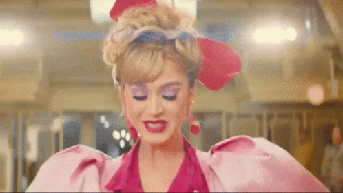 Gif Katy Perry Gif da Katy Perry andando e mandando beijo com uma das mãos. Ela está usando roupa vermelha e rosa.