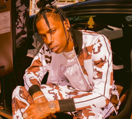 Travis Scott posando para foto com corpo curvado e roupa branca com detalhes em marrom