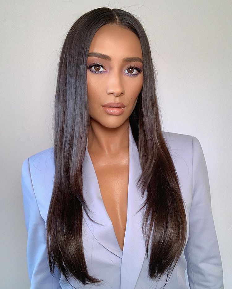 Shay Mitchell veste um blazer azul claro, tem o cabelo liso longo, solto e partido ao meio