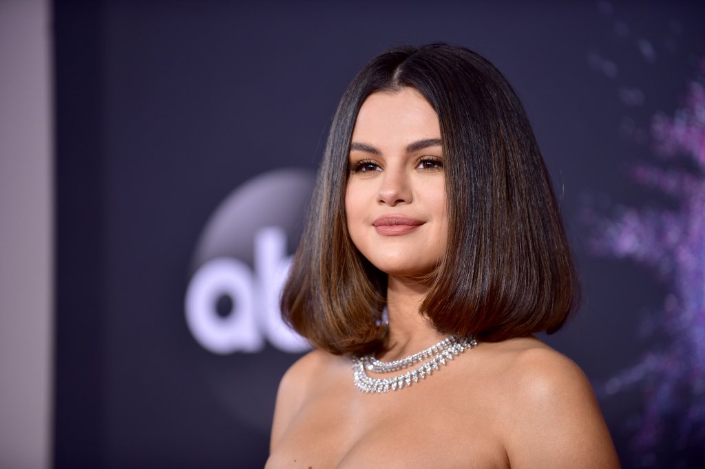 Selena Gomez olhando para o lado com um leve sorriso sem mostrar os dentes. Ela está com um cabelo liso chanel, colar de diamantes e não dá para ver o seu vestido, que não tem alças.