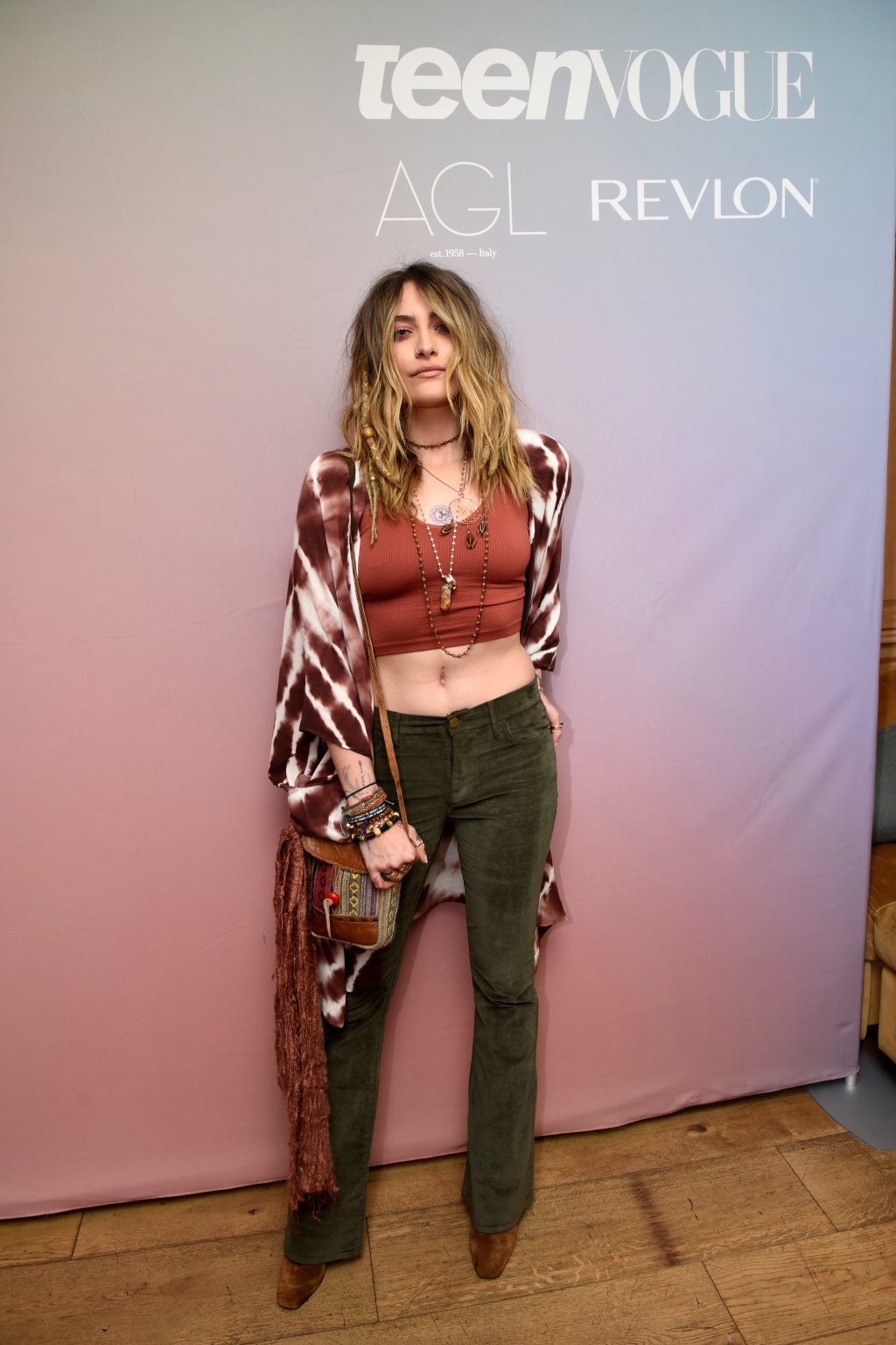 Paris Jackson usando kimono tie-dye, bolsa de franjas, top cropped marrom, calça de veludo verde e bota marrom