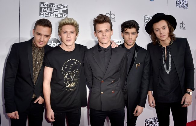 2014 American Music Awards – Red Carpet Foto dos integrantes do One Direction no tapete vermelho posando. Todos estão de preto e Harry está com um chapéu.