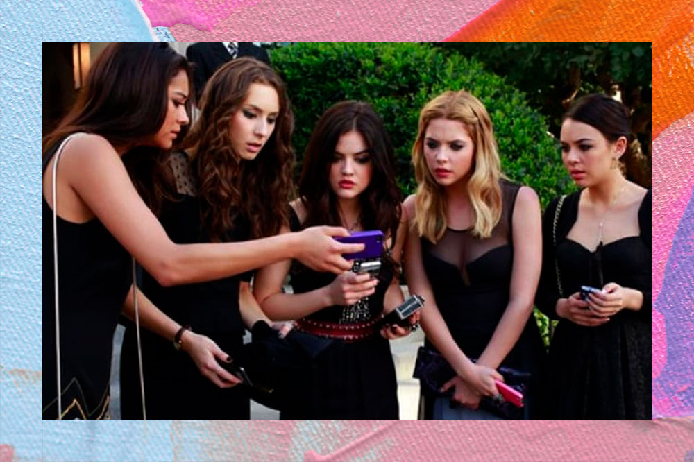 Atrizes de Pretty Little Liars, vestindo roupas pretas, estão em roda olhando assustadas para um celular