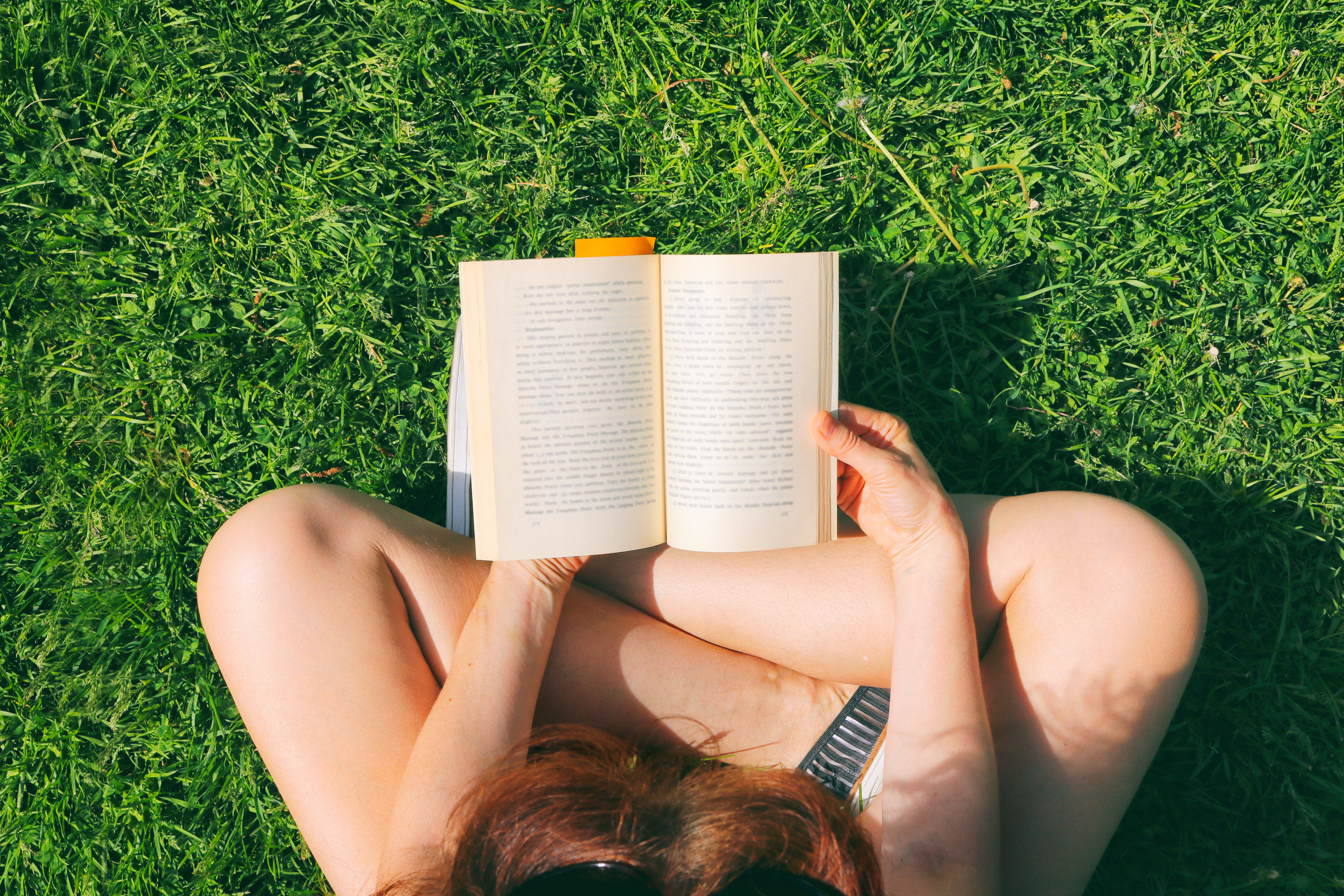 Imagem de uma mulher branca lendo um livro em um gramado.
