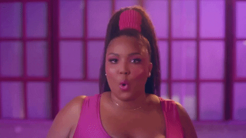 lizzo-tendencia-anos-80 Lizzo, no clipe de Juice, usando body rosa e cabelo preso em um rabo com scrunchie rosa. Ela está apontado para a câmera com o dedo e falando