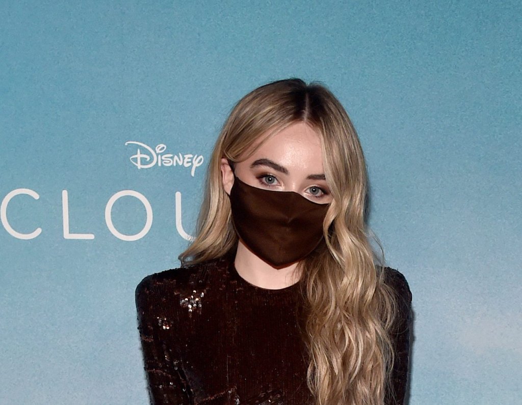 Sabrina Carpenter usando vestido marrom escuro volumoso, assimétrico em camadas de brilhos com salto de plataforma na mesma tonalidade