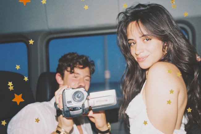 Shawn Mendes e Camila Cabello. Ela olha de lado e sorri enquanto ele segura uma câmera