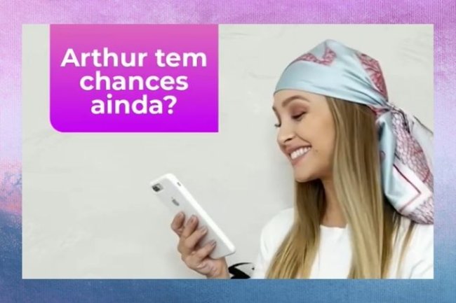 Carla Diaz usa lenço na cabeça, camiseta branca, sorri e segura celular. Na imagem está escrito 