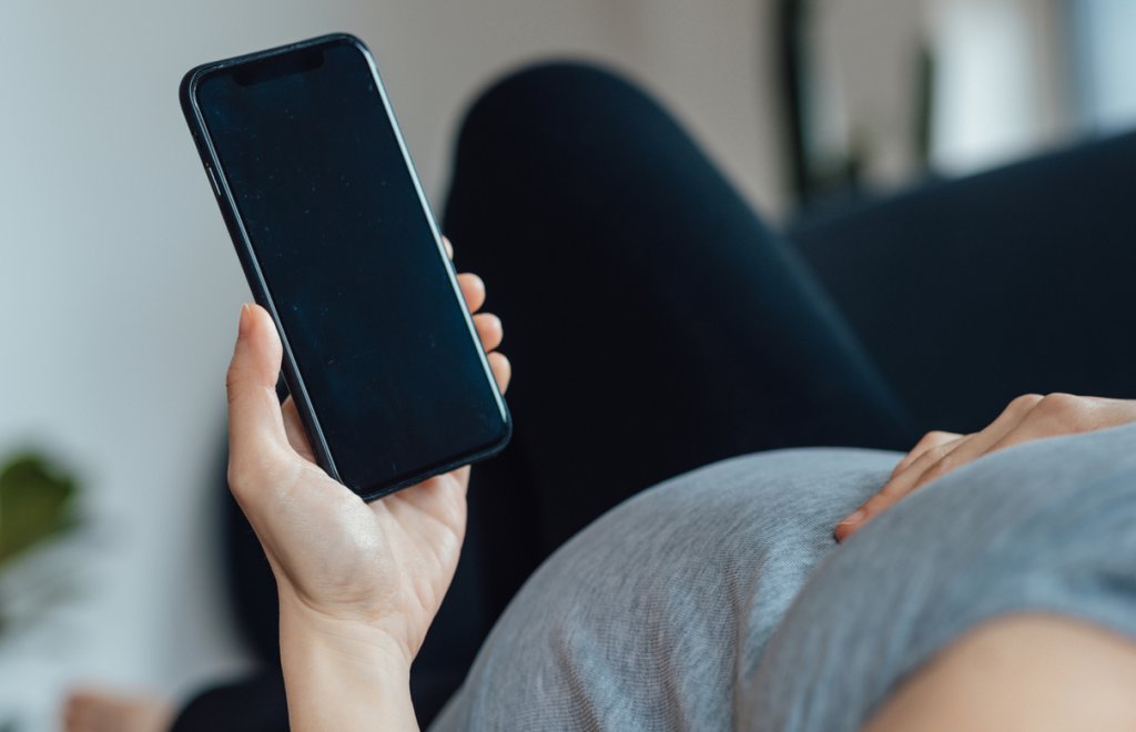 Mulher grávida deitada no sofá segurando um celular