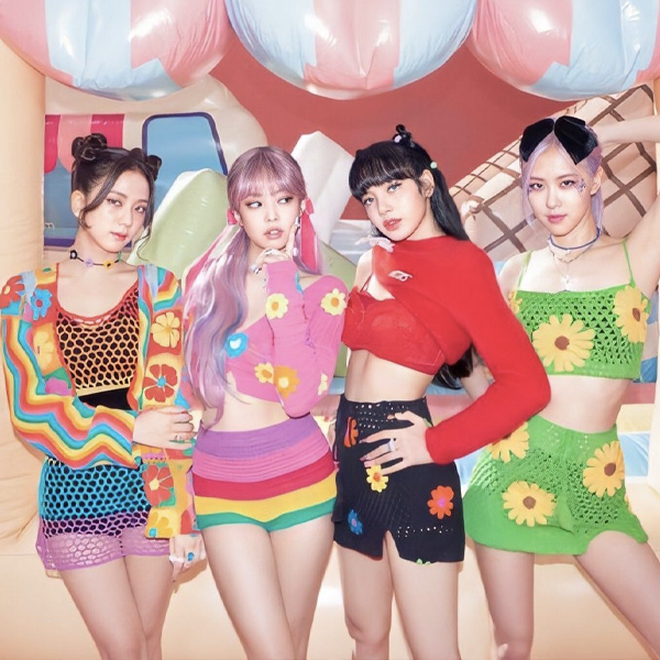 Grupo Blackpink no clipe de Ice Cream parceria com Selena Gomez, as meninas do grupo usam roupas coloridas com listras divertidas, flores, e posam em frente ao cenário que parece uma sorveteria.