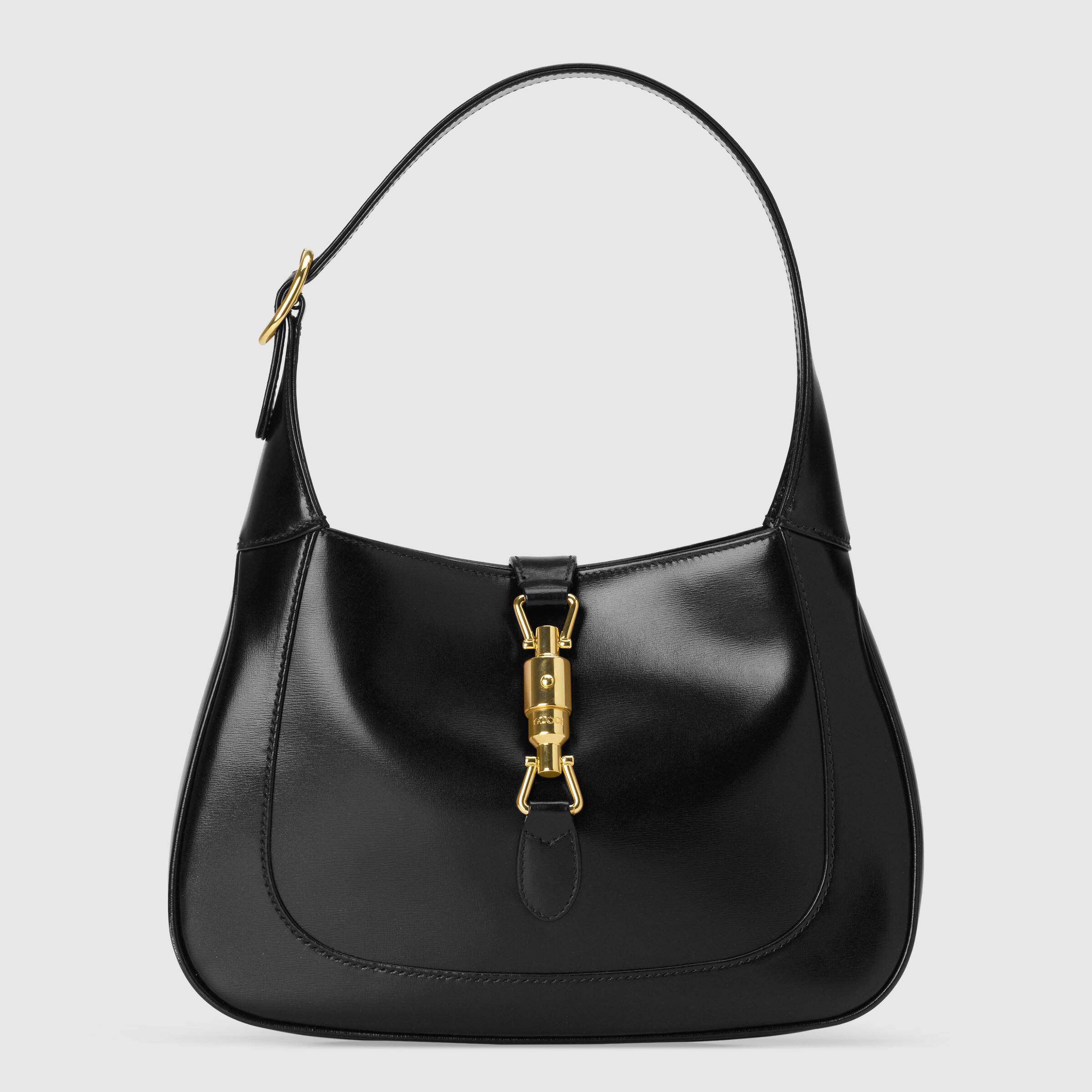 bolsa-gucci-harry-styles Foto da bolsa modelo Jackie 1961, da Gucci, que foi usada por Harry Styles em campanha da marca. A bolsa é preta de couro, tem alça curta, formato arredondado e um fecho dourado na frente. O fundo da foto é liso com tom acizentado.