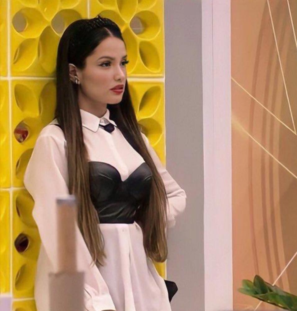 juliette-camisa-corset-bbb21- Juliette Freire no Big Brother Brasil 21 usando camisa branca, corset preto e tiara preta. Ela está encostada em uma parede amarela, com expressão facial séria, e a foto foi tirada de lado.