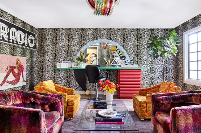 miley8 A imagem mostra uma das salas da casa de Miley Cyrus. A decoração é marcada pelo papel de parede de oncinha, sofás em vermelho e laranja, e um letreiro escrito