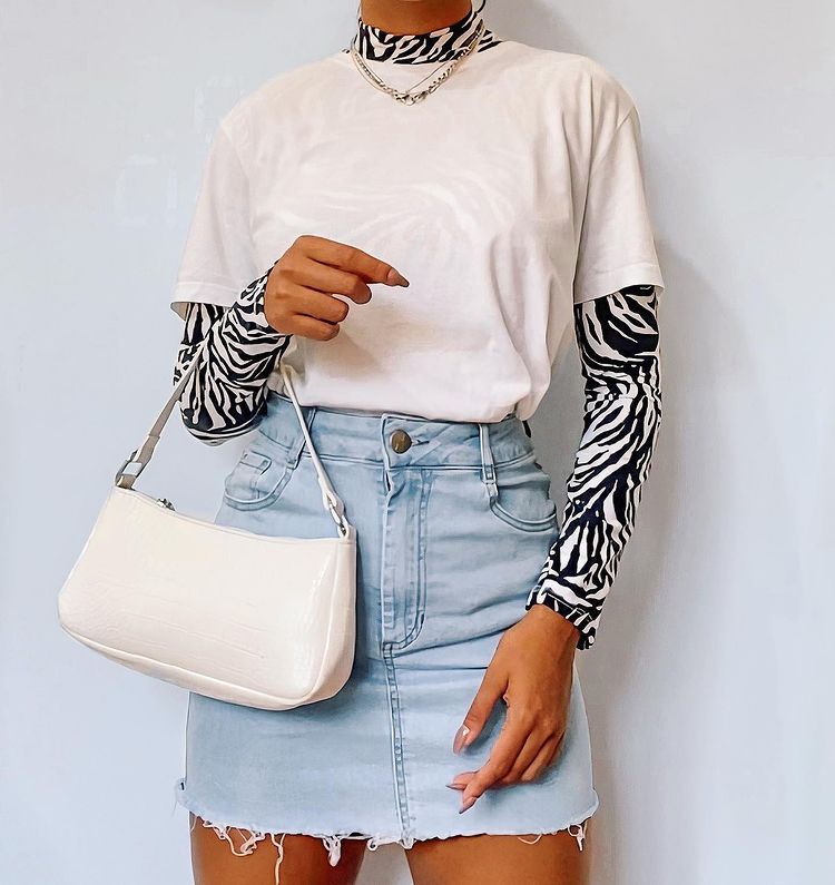 tendencias-outono-inverno-brendapabreu-02 Garota usa blusa segunda pele por baixo de camiseta bege básica, com saia jeans clara e bolsa baguete off-white pendurada em um dos braços. A foto mostra apenas do pescoço para baixo até a altura da coxa.
