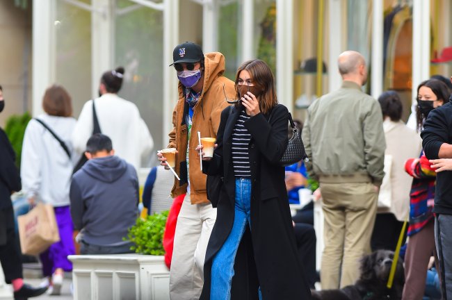 Jacob Elordi e Kaia Gerber andando na rua com café na mão e usando máscara