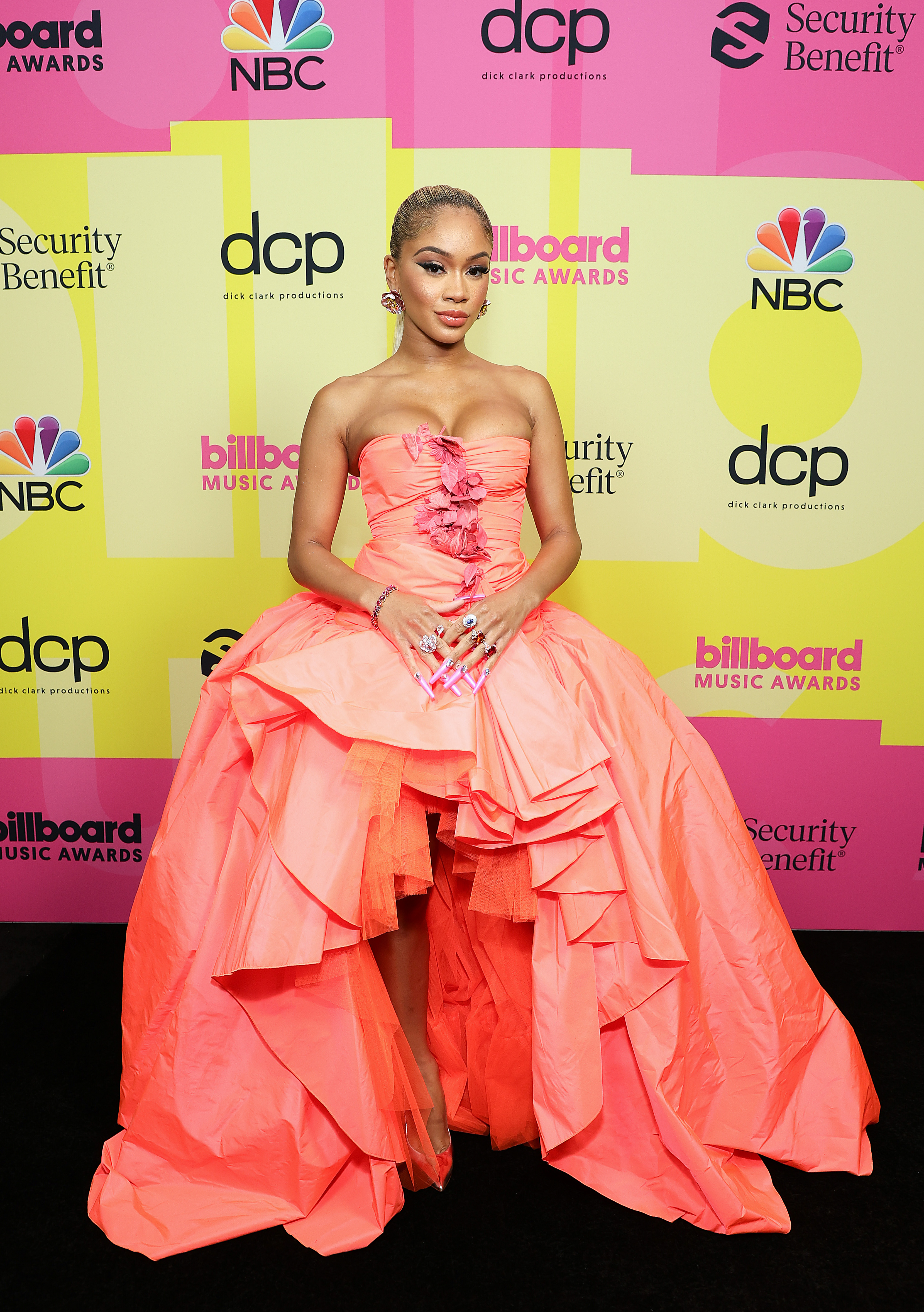 saweetie-billboard-music-awards Saweetie no Billboard Music Awards 2021. Ela está usando um vestido laranja sem alças com saia volumosa e abertura na parte da frente.