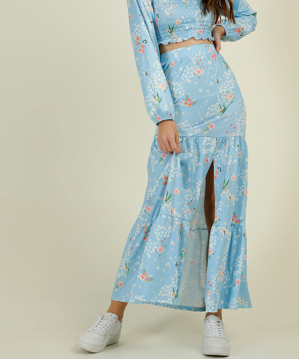 colecao-capricho-marisa-09 Garota usando saia longa floral com fenda da coleção da CAPRICHO com a MARISA com tênis branco. Na foto, só dá para ver da cintura para baixo. Ela está com uma das mãos na cintura, e a outra segurando a saia.