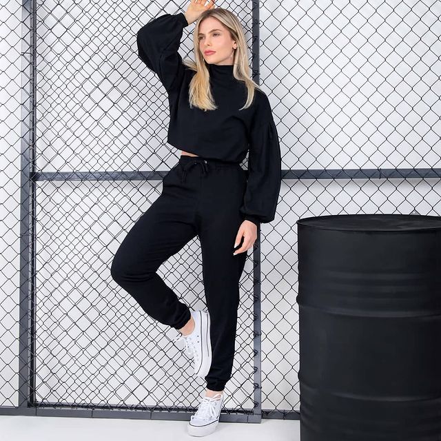 Jovem posando com expressão séria, um dos braços levantados usandoLook monocromático all black com calça jogger