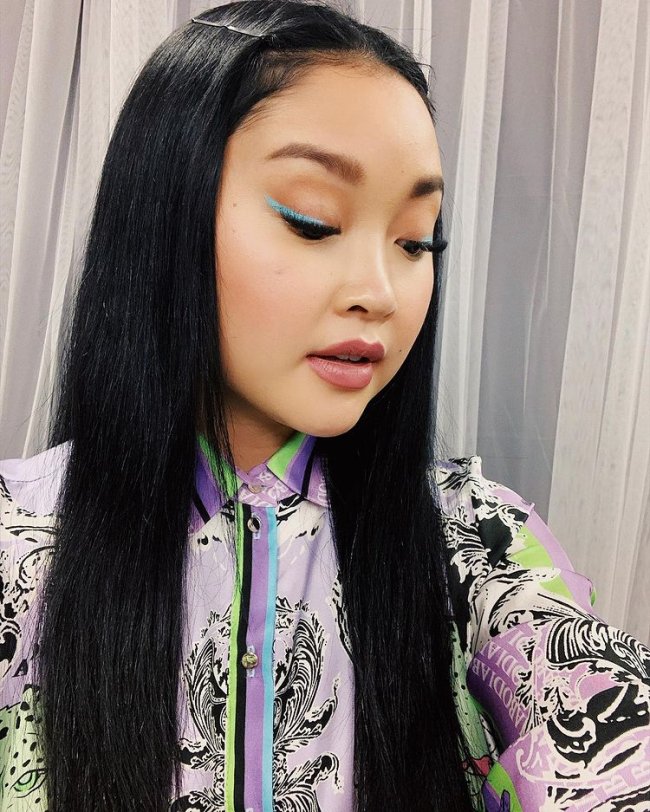 lana condor delineado colorido Selfie da atriz Lana Condor. Ela usa um vestido colorido estampado, cabelo solto, delineado azul e pele natural. Ela olha para baixo e não sorri.