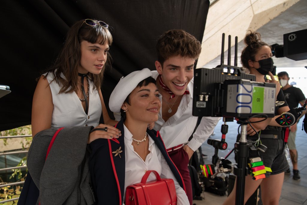 Martina Cariddi, Carla Díaz e Manu Rios nos bastidores de Elite; os dois últimos estão olhando para uma cena no equipamento de filmagem e sorrindo enquanto Martina observa as imagens com atenção e expressão curiosa