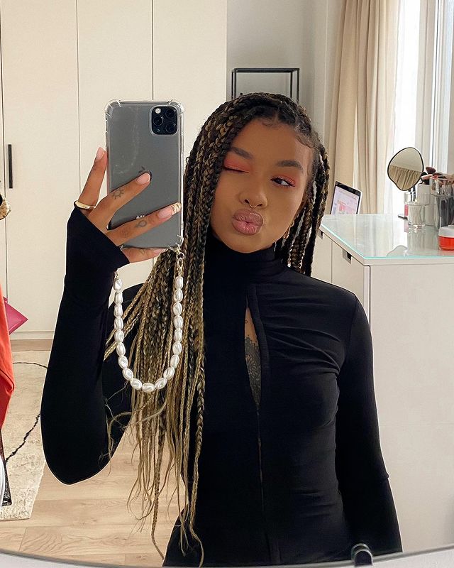 blusa preta de gola alta Selfie no espelho de uma mulher fazendo bico e piscando um olho. Ela usa uma blusa de manga longa e gola alta com um corte no meio dos seios.