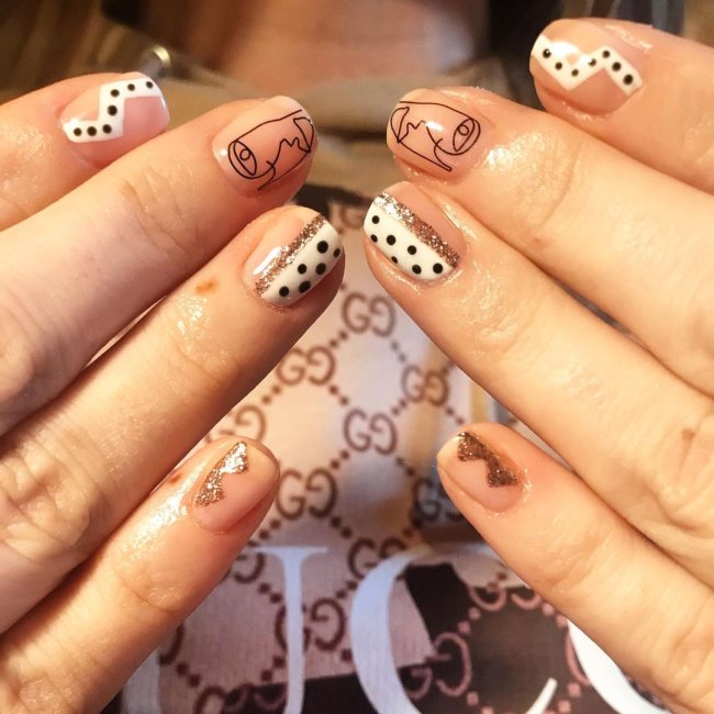 Foto com destaque nas unhas com nail art de bolinha, dessa vez com desenhos abstratos, e algumas unhas com esmalte branco e bolinha preta.