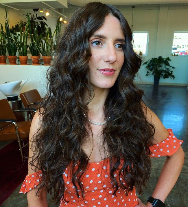 cabelo cacheado com curtain bangs Jovem posando com vestido laranja com bolinhas, ela colocou uma mão na cintura e olha para o lado direito com uma expressão sorridente.