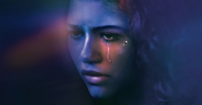 Foto do rosto da personagem Rue da série da HBO, Euphoria. Ela olha para frente, está com uma lágrima escorrendo no olho esquerdo e a fotografia tem tons de azul e roxo.