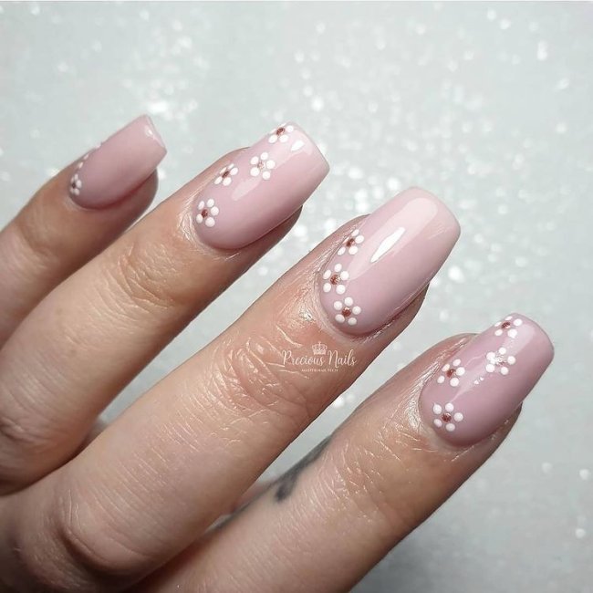 Foto com destaque nas unhas com nail art de bolinha, dessa vez com fundo bege e florzinha no canto inferior da unha.