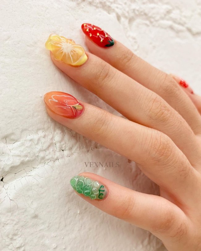 Foto com foco nas unhas com nail art em gel e relevo de frutas.