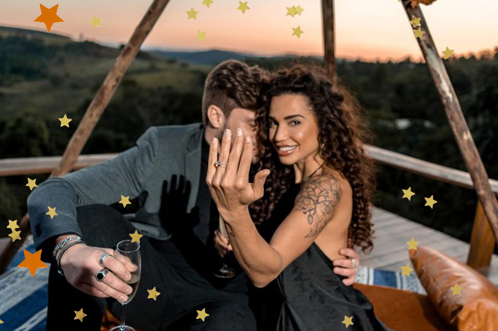 Foto de Paula e Breno do BBB18; ela está sorrindo enquanto mostra o anel de noivado para a câmera enquanto Breno está com o rosto próximo ao pescoço da ex-BBB