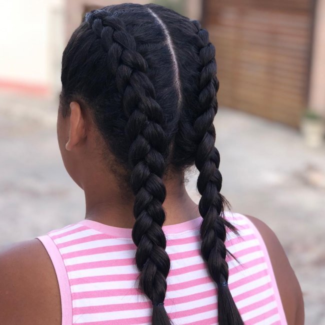 Jovem de costas com camisa listrada em rosa e branco, exibindo trança boxeadora nas laterais da cabeça.