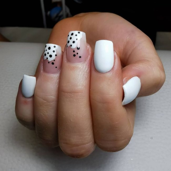 Foto com destaque nas unhas com nail art de bolinha, dessa vez com fundo branco e bolinhas pretas.