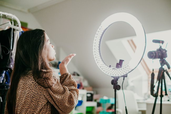 Uma moça, que é influenciadora digital, mandando beijinho pra câmera enquanto grava um conteúdo em seu quarto