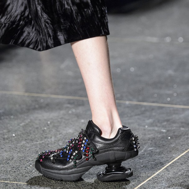 Foto de um tênis preto ortopédico com detalhes de pedras coloridas e salto diferente da Christopher Kane’s x Z-Coil em uma passarela.