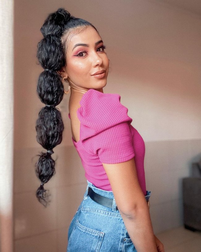 cabelo bubble cacheado Jovem posando de lado usando blusa rosa e trança bolha, sua expressão é séria.