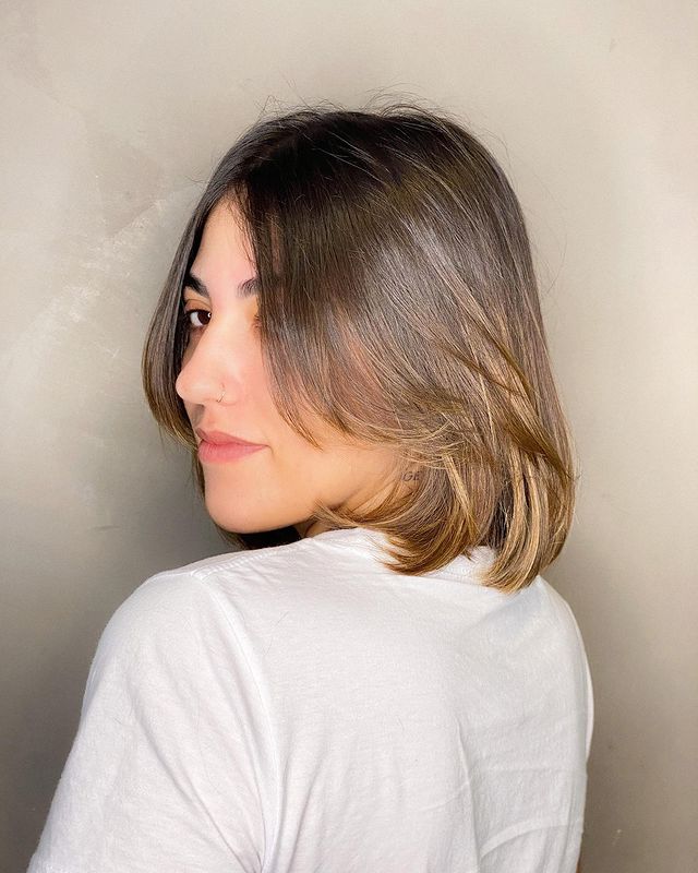 corte chanel Jovem posando virada de lado e com camisa branca, sua expressão é séria.