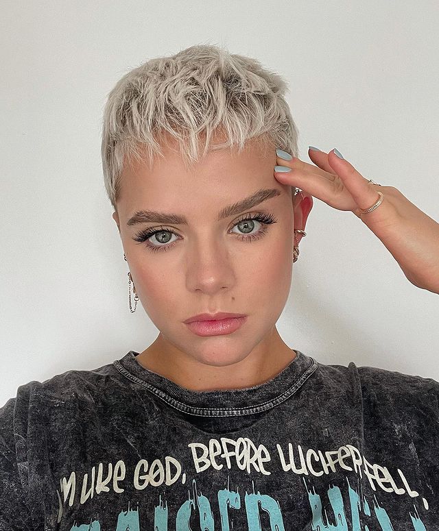 Jovem de camiseta cinza, posando para foto com expressão séria e uma das mãos apoiada no rosto.