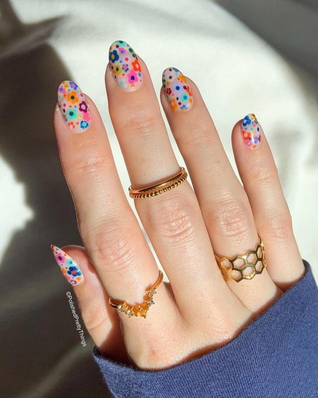 Foto com close nas unhas e tem nail art com desenho de flores coloridas, nas cores rosa, verde, laranja, azul e roxo.