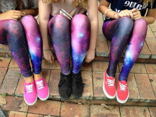 legging-galaxia Foto da perna de três meninas sentadas em uma escada. Todas usam o mesmo modelo de calça legging com estampa de galaxia e tênis.