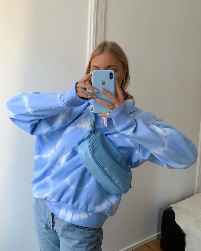 look-moletom-tye-die Selfie no espelho de uma mulher. Ela usa um moletom tie dye azul, calça jeans e bolsa azul.