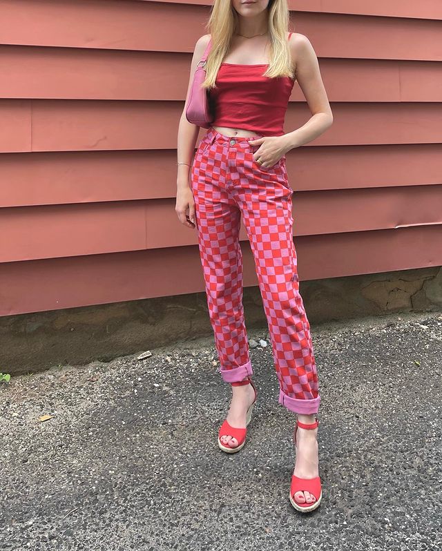 look quadriculado rosa e vermelho Na imagem só podemos ver dos ombros para baixo, ela usa uma regata vermelha e calça quadriculada vermelha e rosa com salto rosa.
