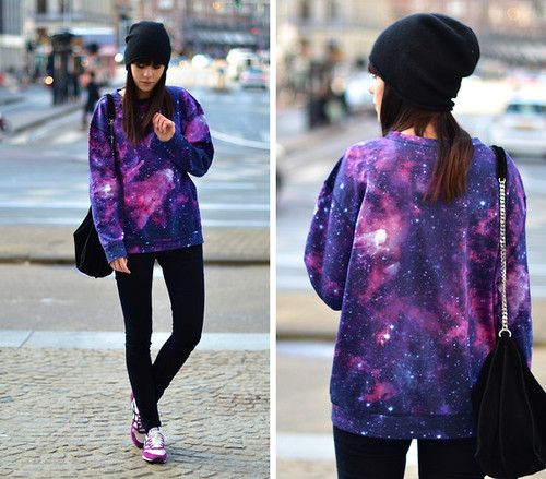 moletom-galaxia Montagem de duas fotos da mesma garota usando um moletom de galaxia em ângulos diferentes. Ela usa um gorro preto, moletom, calça preta e um tênis branco e roxo. Ela não olha para a câmera.