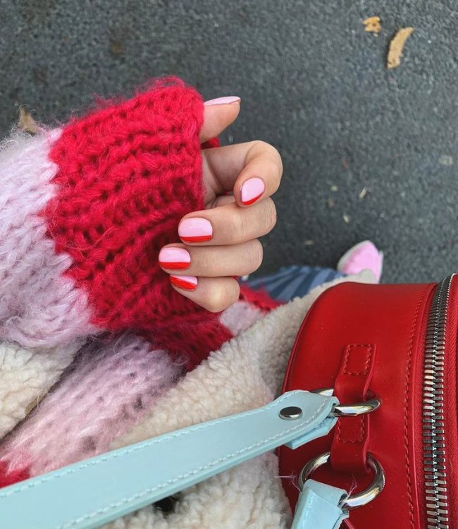 Foto com foco nas mãos mostrando nail art rosa com detalhes vermelhos. Também podemos ver uma parte da blusa de tricô com detalhes em vermelho e rosa e uma parte da bolsa na cor vermelha.